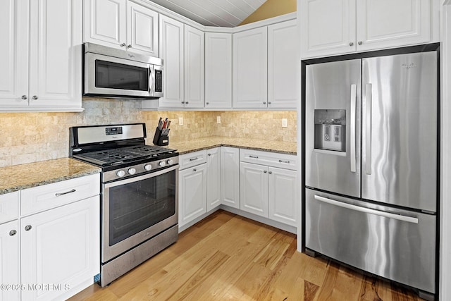 kitchen featuring light hardwood / wood-style flooring, appliances with stainless steel finishes, light stone countertops, white cabinets, and decorative backsplash