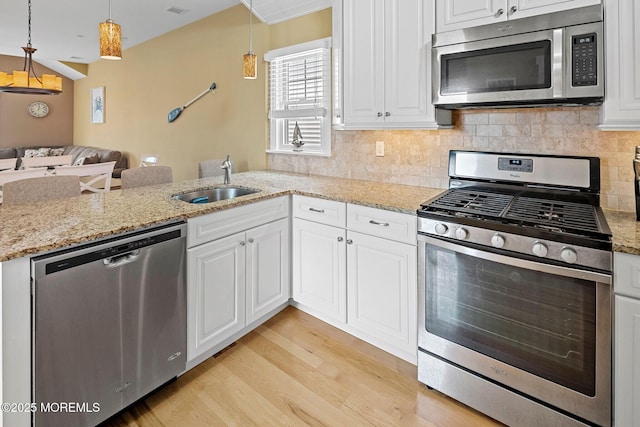 kitchen with pendant lighting, sink, stainless steel appliances, white cabinets, and light wood-type flooring