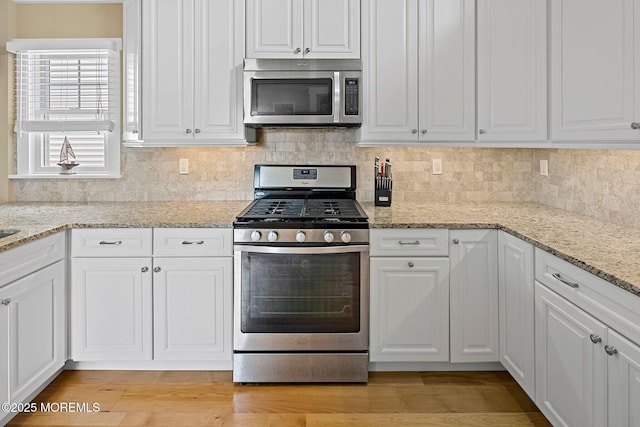 kitchen with appliances with stainless steel finishes, light stone countertops, light hardwood / wood-style flooring, and white cabinets