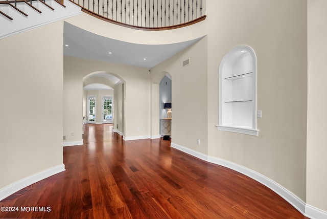 unfurnished room with built in shelves, a towering ceiling, and hardwood / wood-style floors