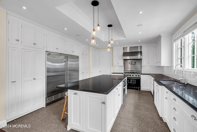 kitchen featuring wall chimney exhaust hood, sink, a center island, premium appliances, and pendant lighting