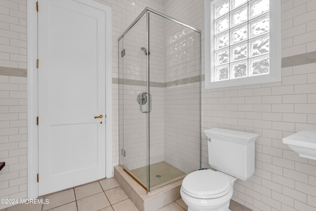 bathroom with tile patterned flooring, tile walls, an enclosed shower, and toilet