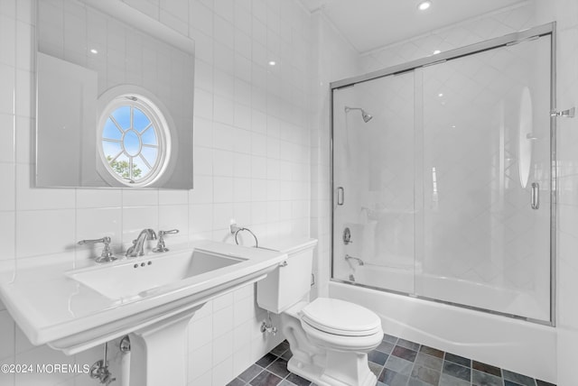 full bathroom with toilet, sink, combined bath / shower with glass door, tile walls, and decorative backsplash