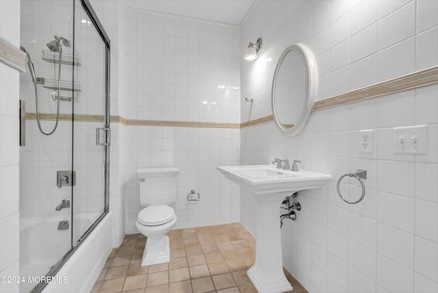 bathroom with combined bath / shower with glass door, tile walls, tile patterned floors, and toilet