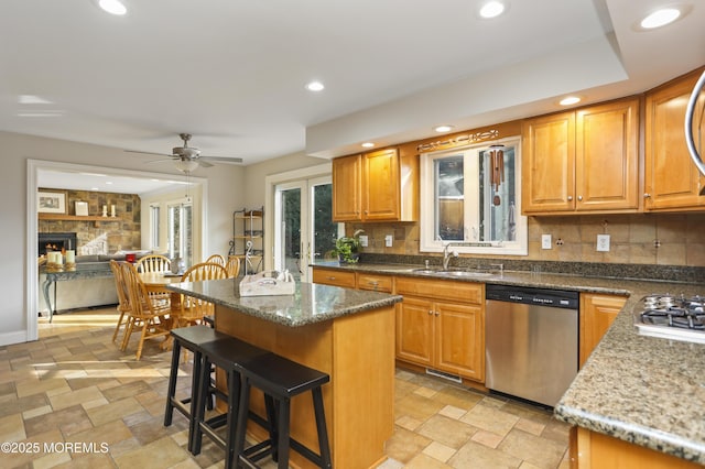 kitchen with sink, stone countertops, appliances with stainless steel finishes, a kitchen island, and a fireplace