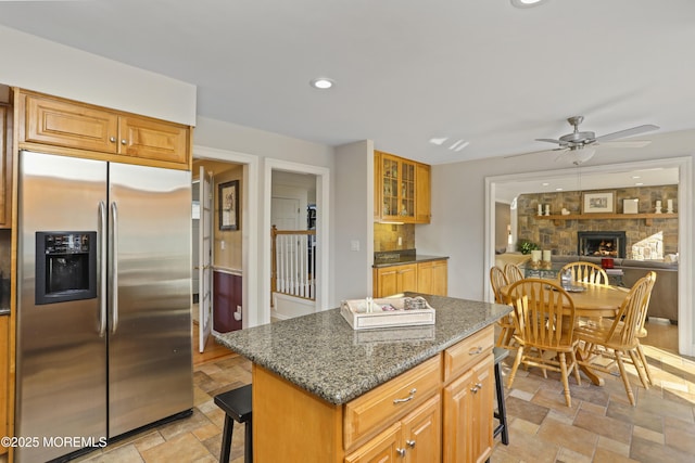 kitchen featuring dark stone countertops, a kitchen breakfast bar, a fireplace, a kitchen island, and stainless steel fridge with ice dispenser