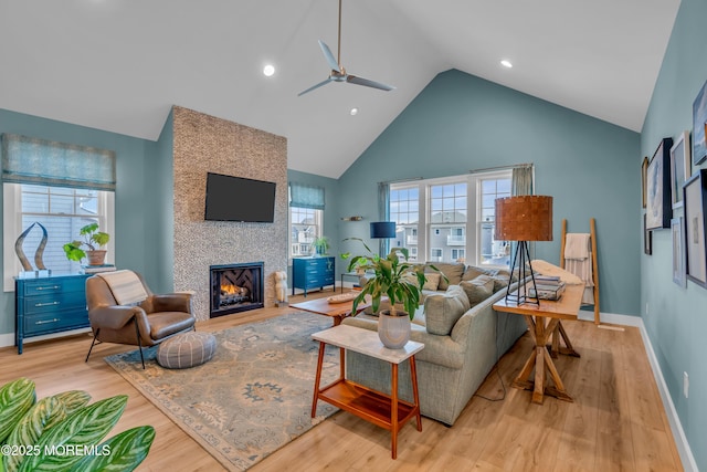 living room featuring ceiling fan, a large fireplace, high vaulted ceiling, and light wood-type flooring