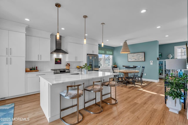 kitchen featuring white cabinetry, appliances with stainless steel finishes, wall chimney exhaust hood, and an island with sink