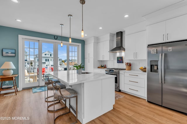 kitchen featuring white cabinets, hanging light fixtures, a center island, stainless steel appliances, and wall chimney exhaust hood