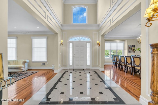 entrance foyer featuring ornamental molding, a towering ceiling, an inviting chandelier, and light hardwood / wood-style floors