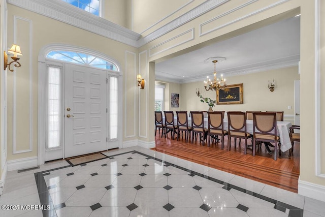 tiled entrance foyer with ornamental molding, a towering ceiling, and an inviting chandelier