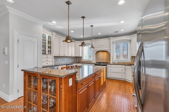 kitchen featuring a kitchen island, hanging light fixtures, ornamental molding, light stone counters, and stainless steel appliances