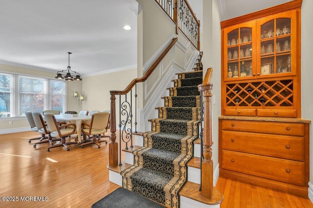 stairs featuring a notable chandelier, wood-type flooring, and ornamental molding