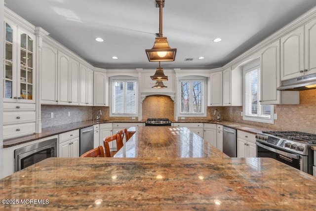 kitchen featuring appliances with stainless steel finishes, pendant lighting, tasteful backsplash, white cabinetry, and dark stone countertops