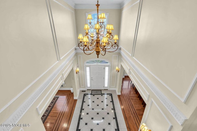 tiled entryway featuring a towering ceiling, ornamental molding, and a chandelier