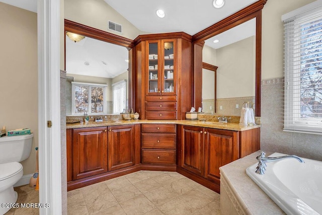 bathroom featuring vanity, a wealth of natural light, tiled bath, and toilet