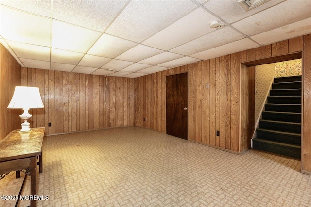 basement featuring a drop ceiling and wooden walls
