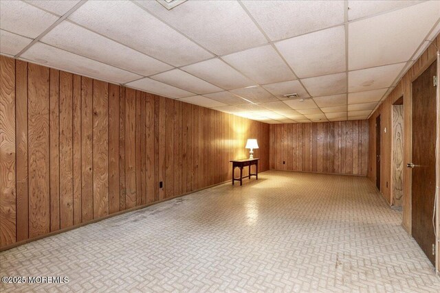 basement with a paneled ceiling and wood walls