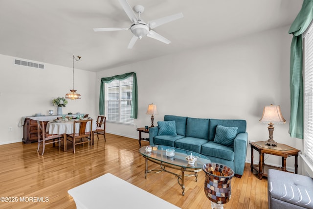 living room featuring a ceiling fan, light wood-type flooring, visible vents, and baseboards