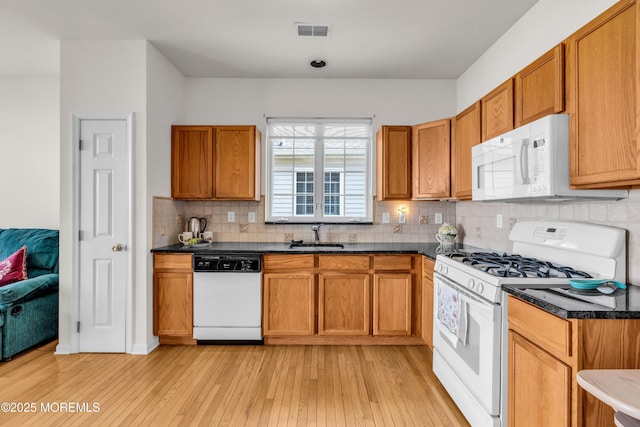 kitchen with light wood finished floors, white appliances, dark countertops, and visible vents