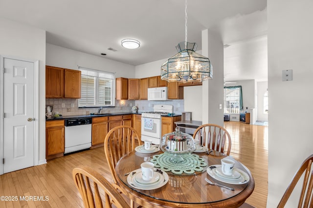 kitchen featuring white appliances, a sink, light wood-type flooring, decorative backsplash, and dark countertops