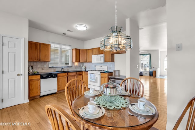 kitchen with brown cabinets, tasteful backsplash, light wood-style flooring, a sink, and white appliances