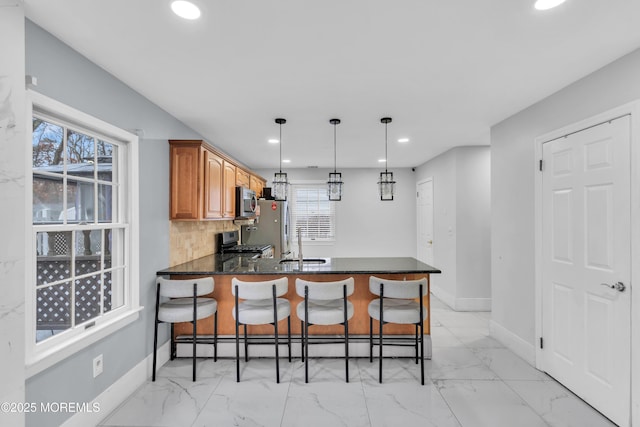 kitchen featuring pendant lighting, appliances with stainless steel finishes, backsplash, a kitchen breakfast bar, and kitchen peninsula