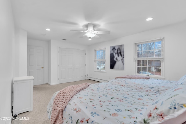 bedroom with multiple windows, a baseboard heating unit, light colored carpet, and a closet