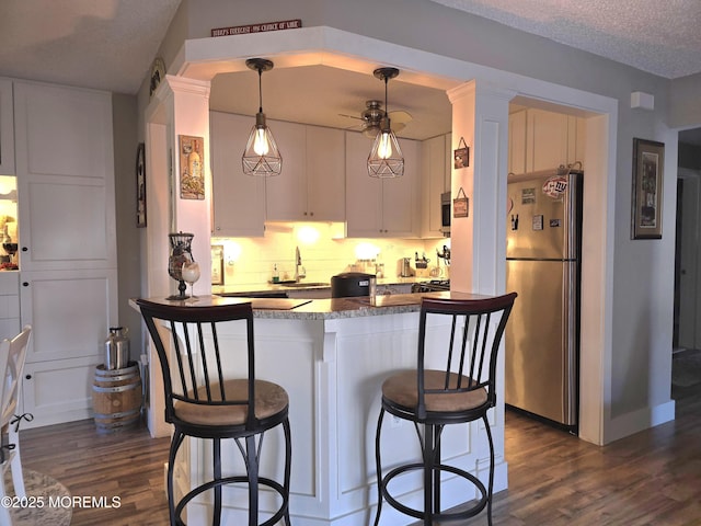 kitchen featuring dark wood-type flooring, appliances with stainless steel finishes, kitchen peninsula, pendant lighting, and white cabinets