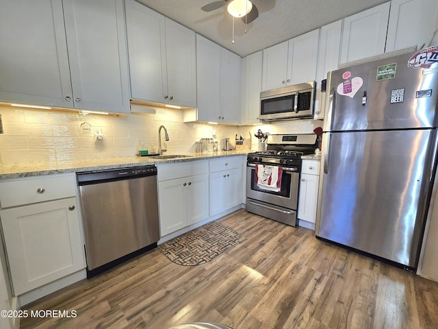 kitchen with appliances with stainless steel finishes, white cabinetry, sink, light stone counters, and light hardwood / wood-style floors