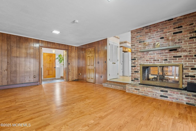 unfurnished living room featuring ornamental molding, a brick fireplace, light wood-type flooring, and wood walls