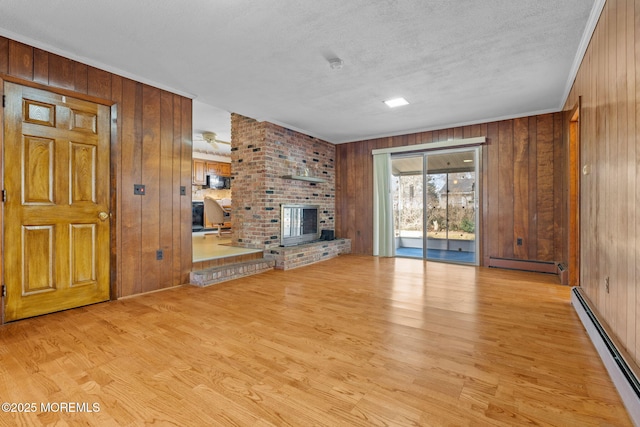 unfurnished living room featuring wood walls, a fireplace, baseboard heating, and light hardwood / wood-style flooring