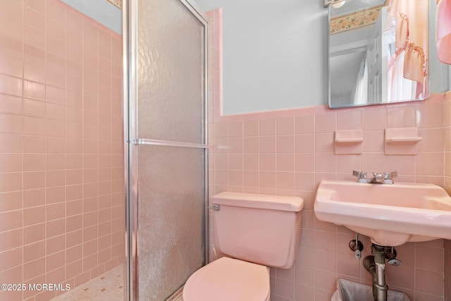 bathroom featuring a shower with shower door, tile walls, and toilet