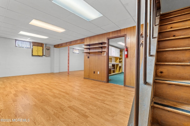 basement featuring a drop ceiling, hardwood / wood-style floors, and wood walls