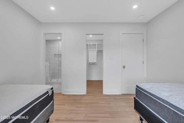 bedroom with ensuite bathroom, a spacious closet, a closet, and light wood-type flooring