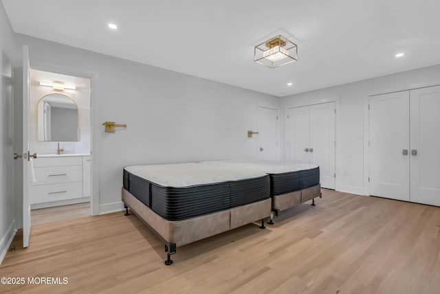 bedroom with two closets, light hardwood / wood-style flooring, and ensuite bath