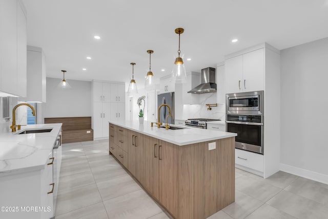 kitchen featuring wall chimney range hood, sink, white cabinetry, stainless steel appliances, and a spacious island