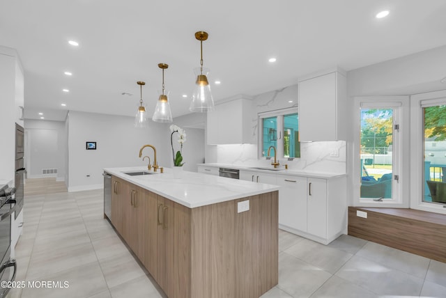 kitchen featuring white cabinetry, sink, an island with sink, and decorative light fixtures