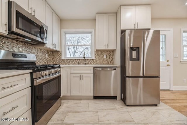 kitchen with appliances with stainless steel finishes, sink, white cabinets, and backsplash