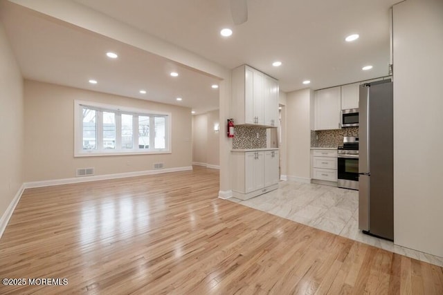 kitchen with tasteful backsplash, light wood-type flooring, white cabinets, and appliances with stainless steel finishes