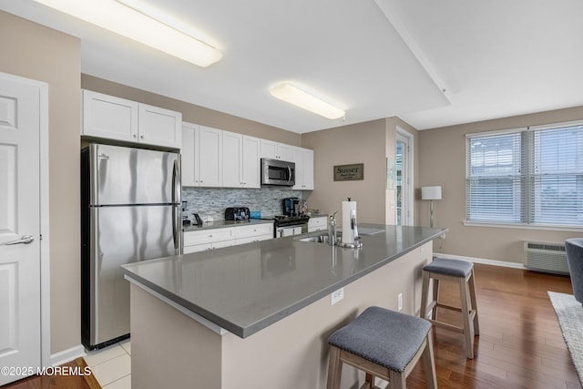 kitchen featuring stainless steel appliances, an island with sink, white cabinets, and a breakfast bar