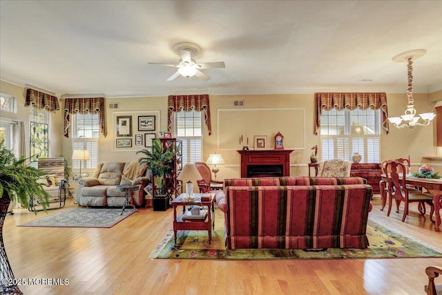 living room featuring ornamental molding, plenty of natural light, ceiling fan with notable chandelier, and light wood-type flooring