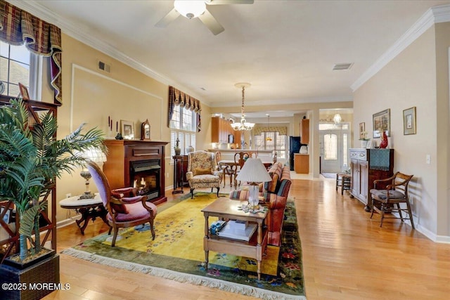 living room with crown molding, ceiling fan with notable chandelier, and light hardwood / wood-style floors