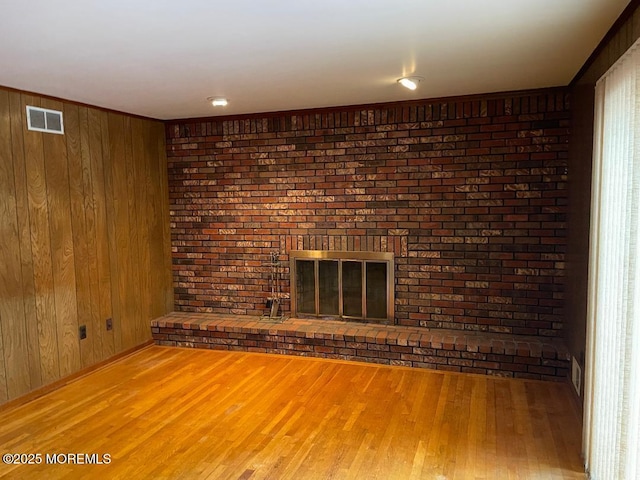 unfurnished living room with hardwood / wood-style flooring, wooden walls, and a fireplace