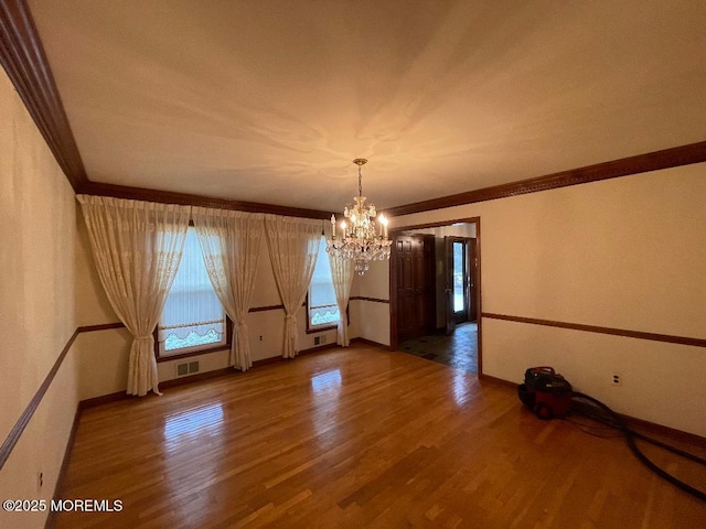 empty room with crown molding, hardwood / wood-style floors, and a notable chandelier