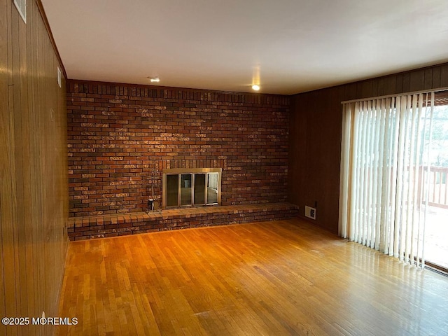 unfurnished living room featuring brick wall, wooden walls, hardwood / wood-style floors, and a fireplace