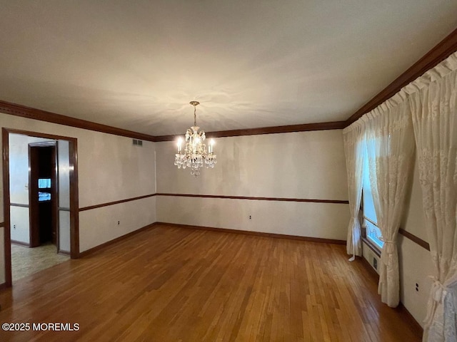 unfurnished room featuring crown molding, hardwood / wood-style floors, and a chandelier