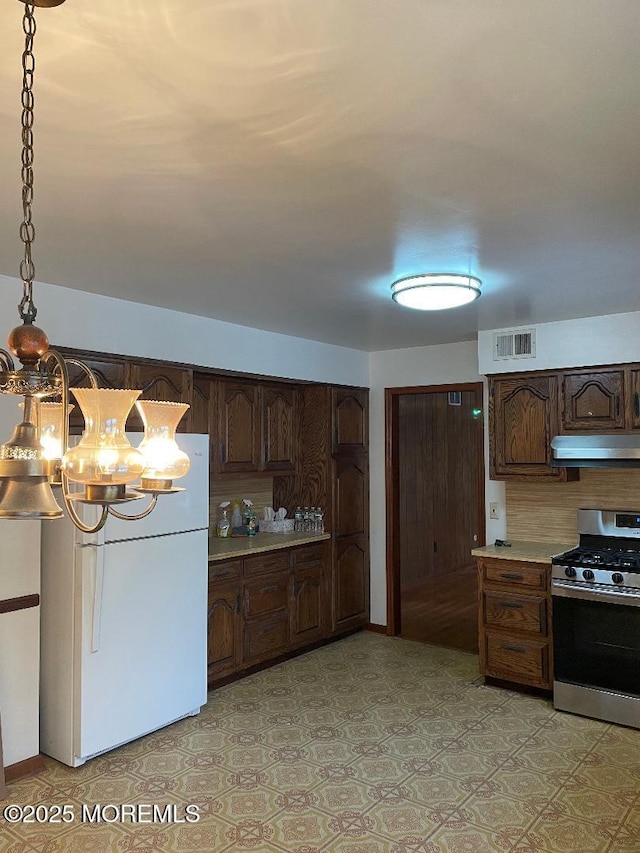 kitchen with pendant lighting, backsplash, dark brown cabinets, white refrigerator, and gas range