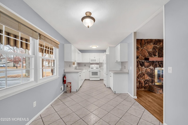 kitchen featuring sink, white appliances, light tile patterned floors, white cabinets, and a stone fireplace