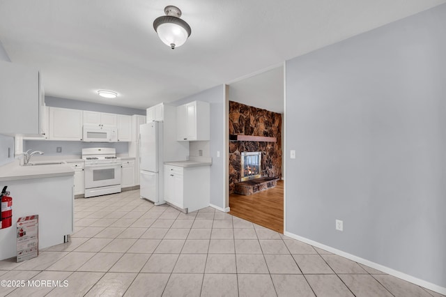 kitchen featuring light tile patterned flooring, a stone fireplace, white cabinetry, sink, and white appliances